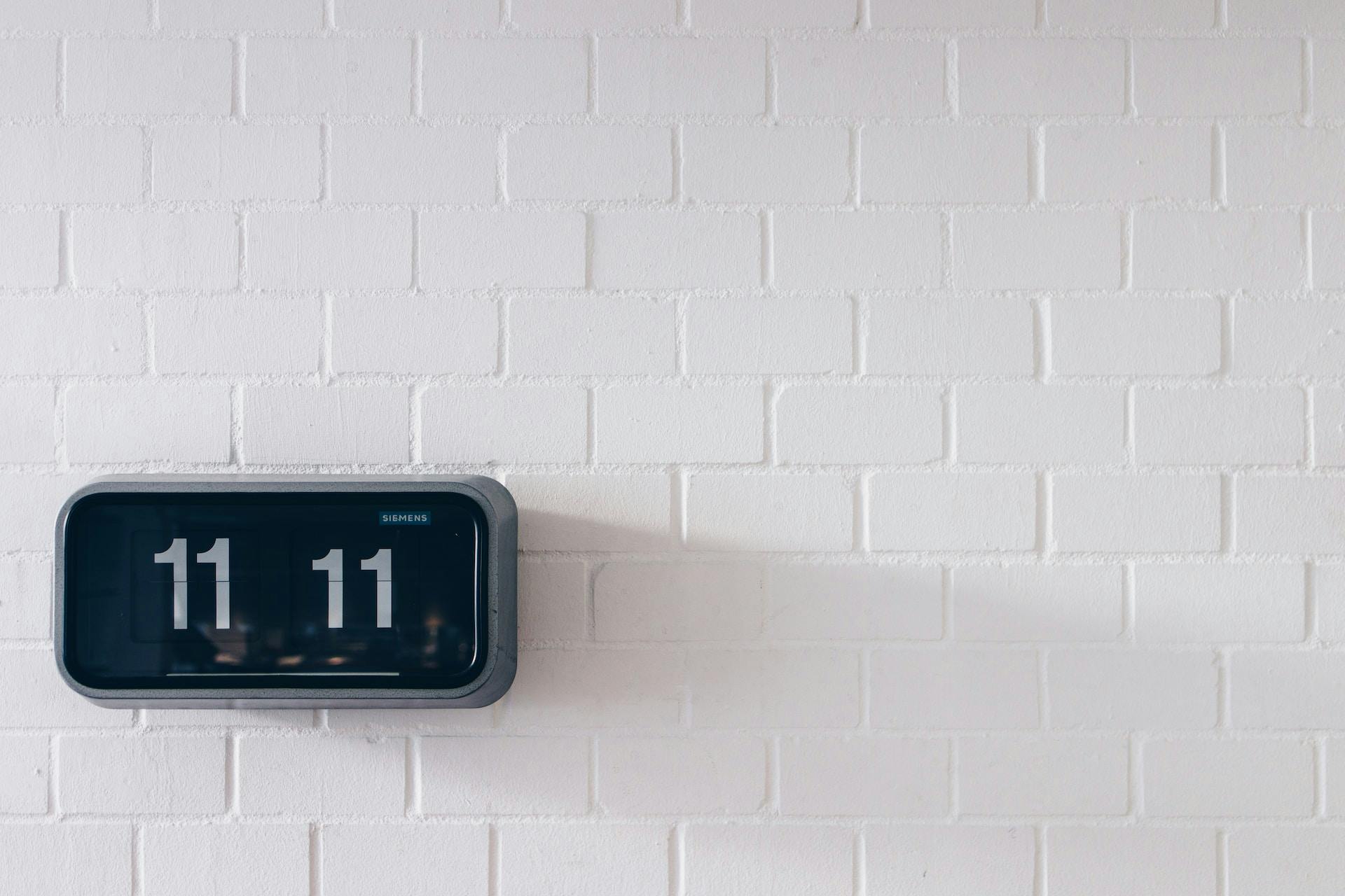 A digital clock on a white brick wall displaying the time 11:11