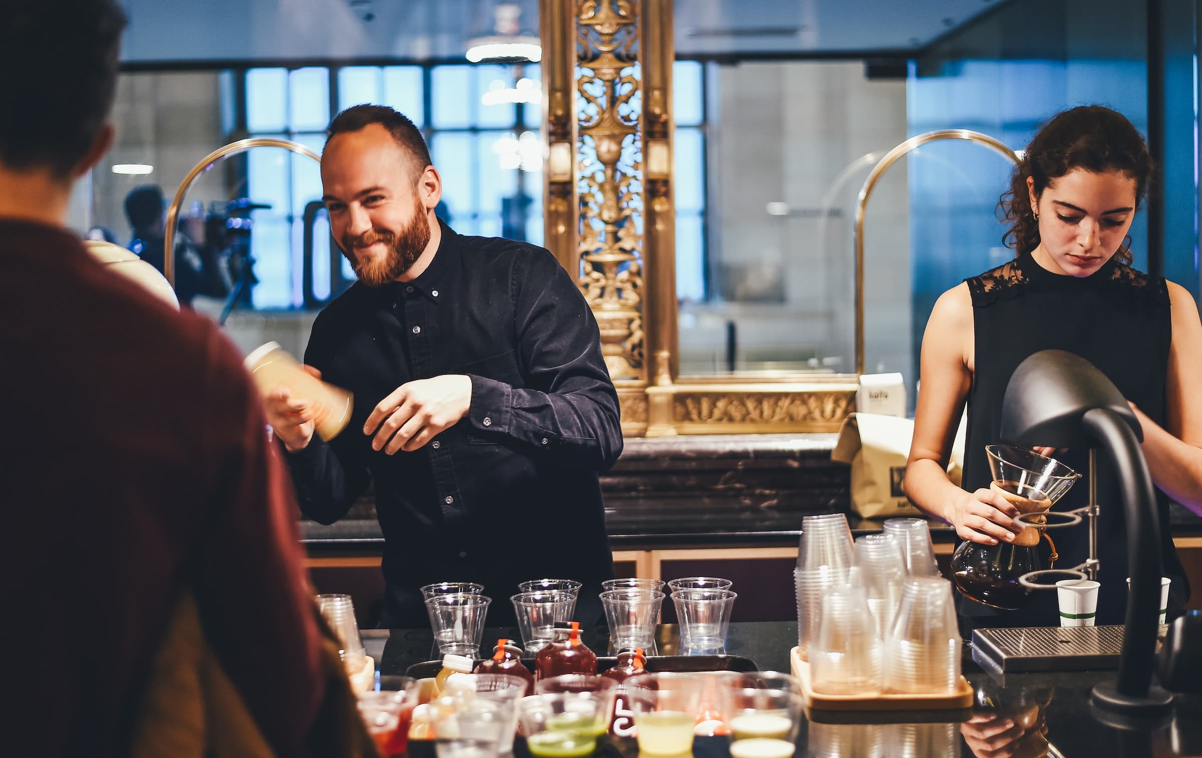 Two baristas mixing beverages and interacting with patrons