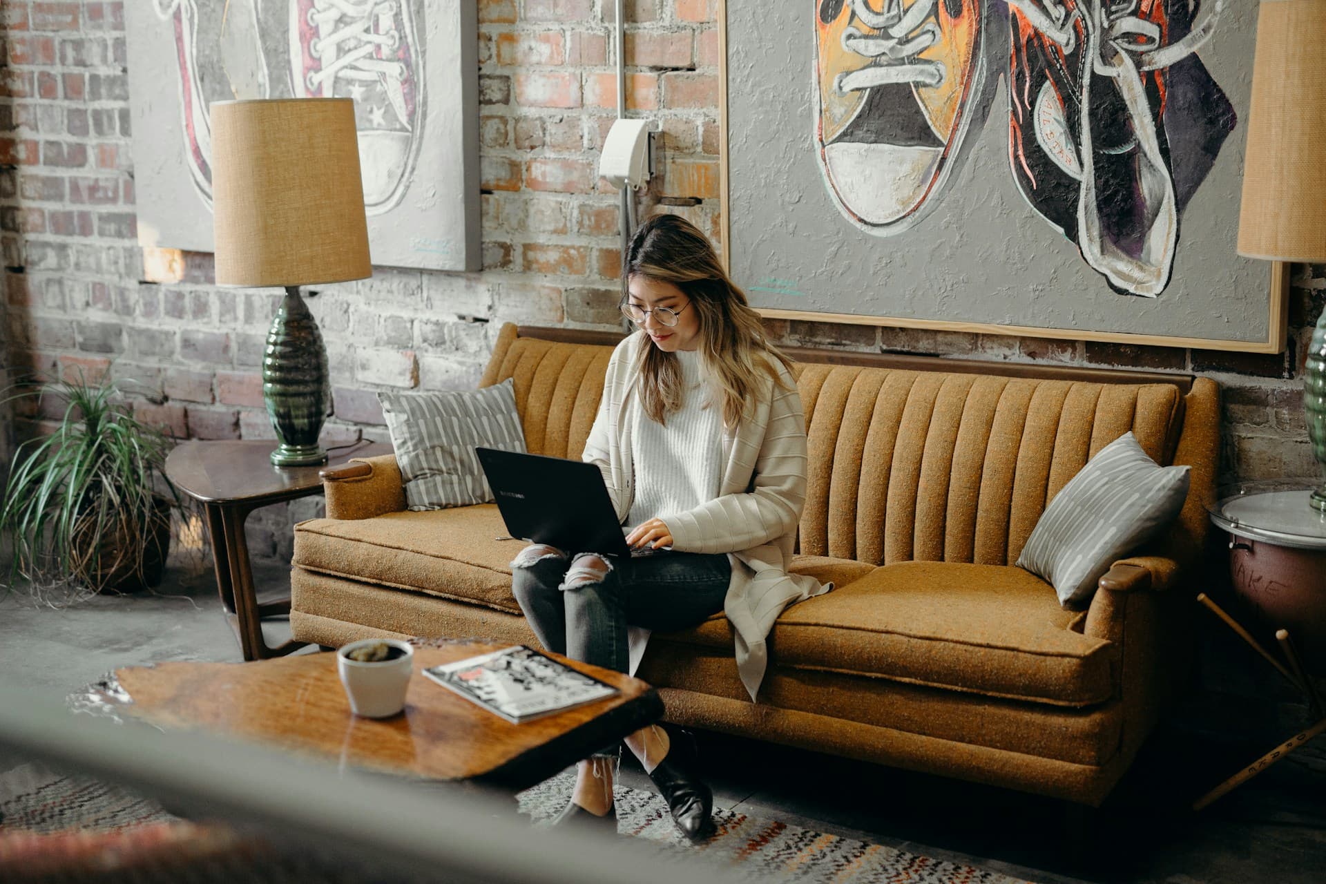 A woman sitting on a couch in a coffee shop, typing on her laptop.