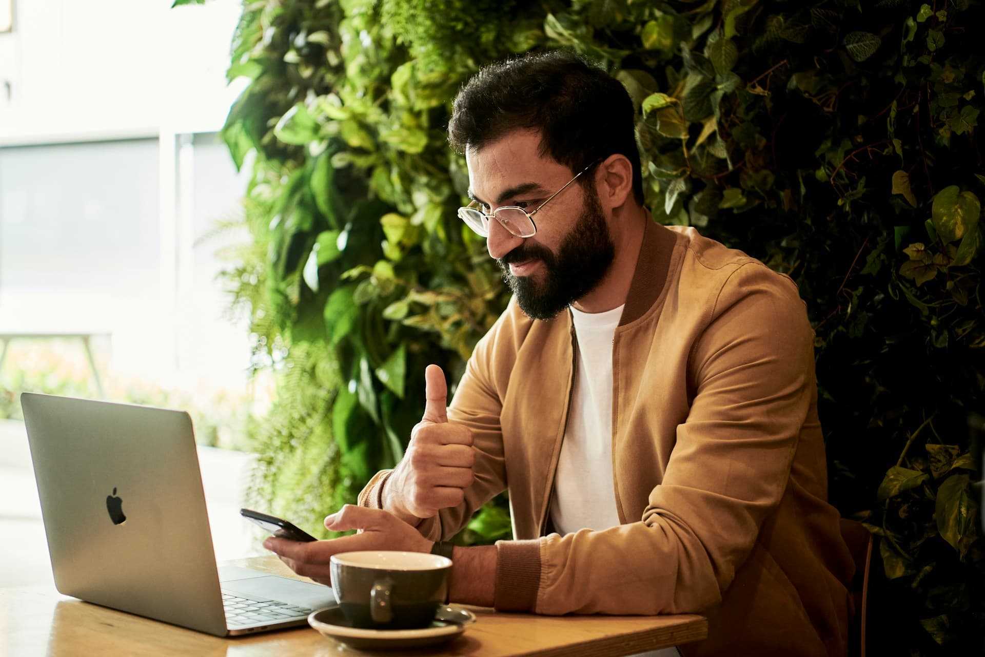 A man smiling at a laptop screen, giving a thumbs up.