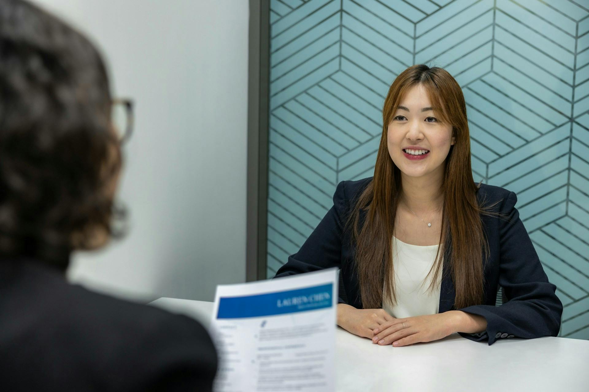 A smiling candidate sitting across a recruiter holding a resume