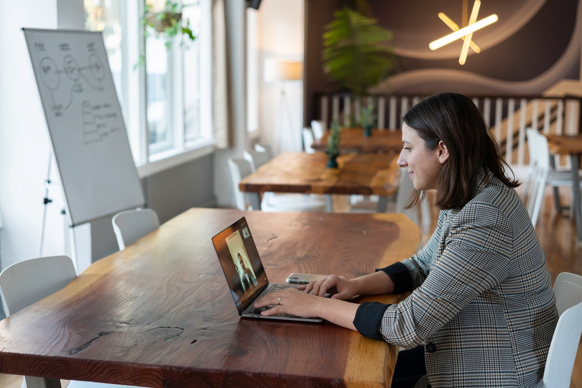 A smiling woman sitting at a table with a laptop, on a video call.