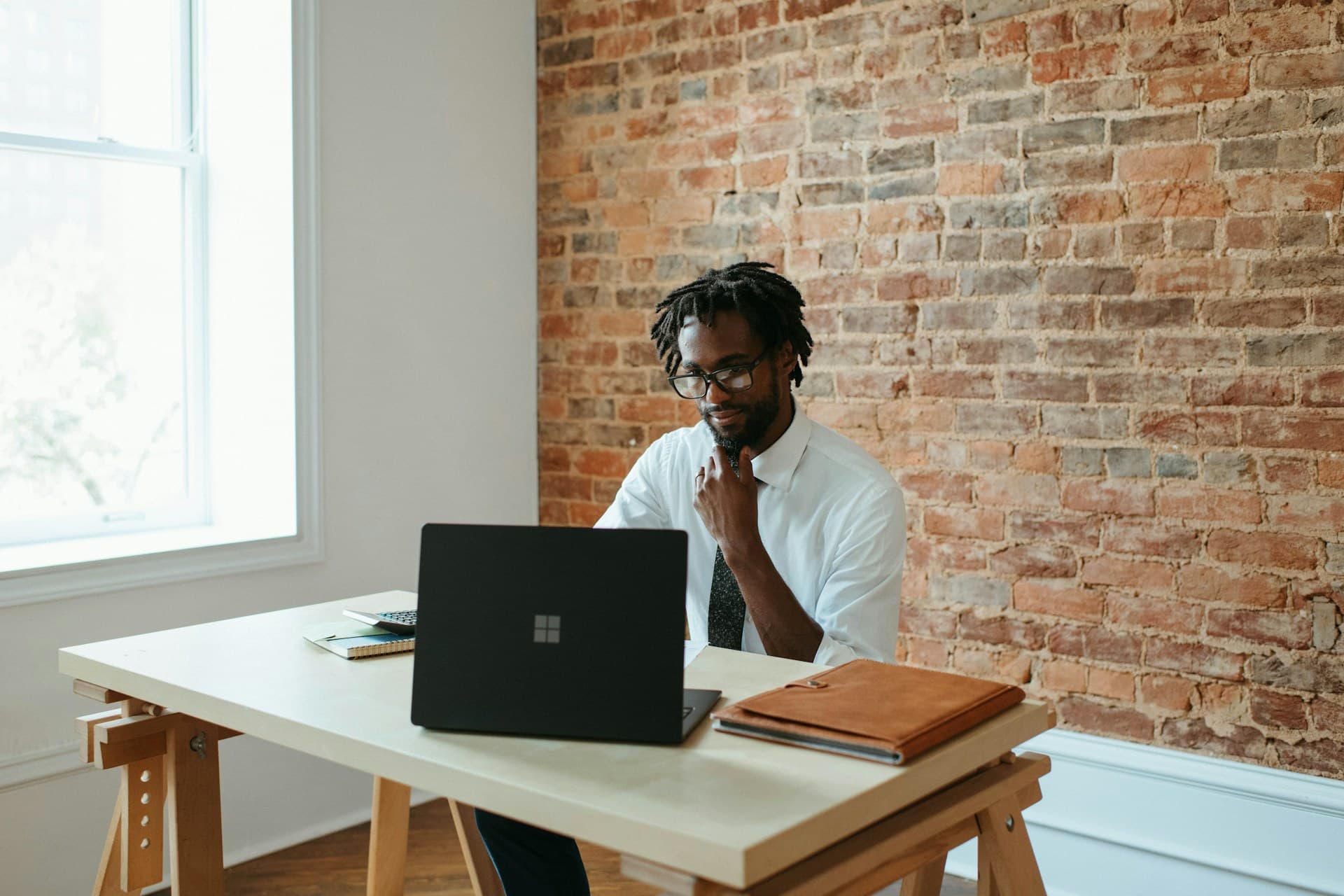 Man sitting at his desk, looking at a laptop screen and stroking his chin