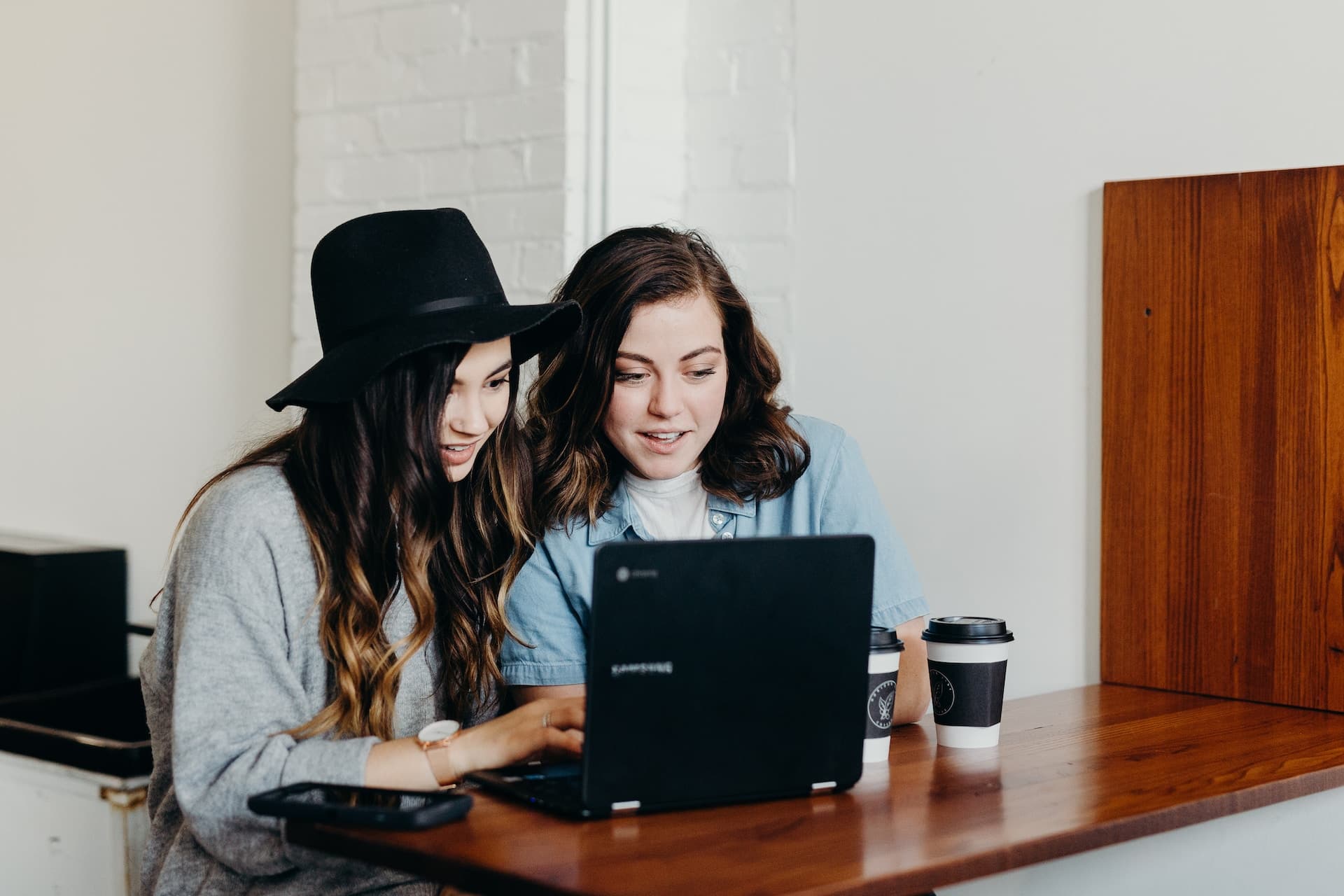 Two women sitting at a table, looking at a laptop screen