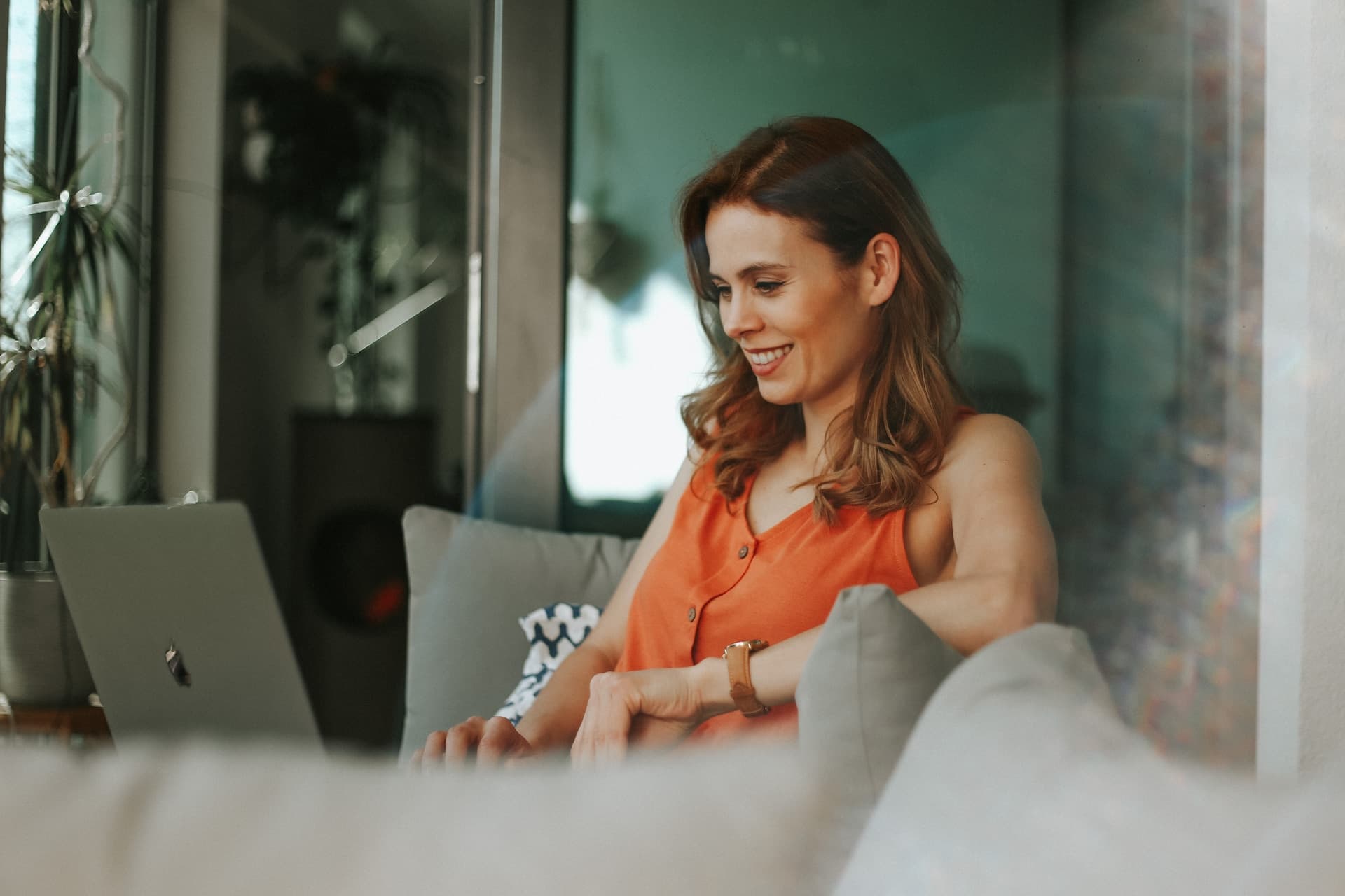 A smiling woman sitting on a couch with a laptop on her lap