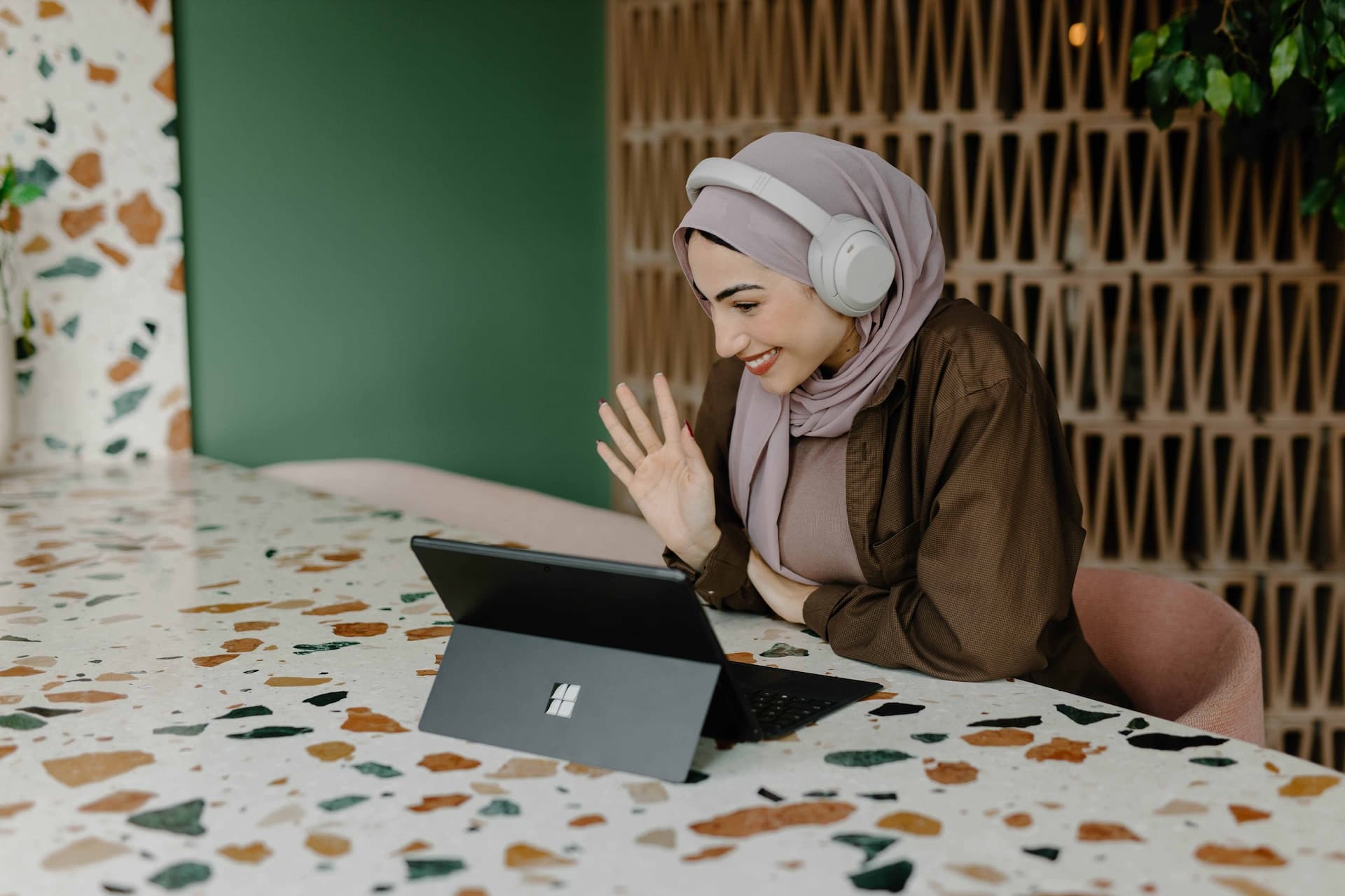 A woman wearing headphones, waving and smiling at her laptop camera