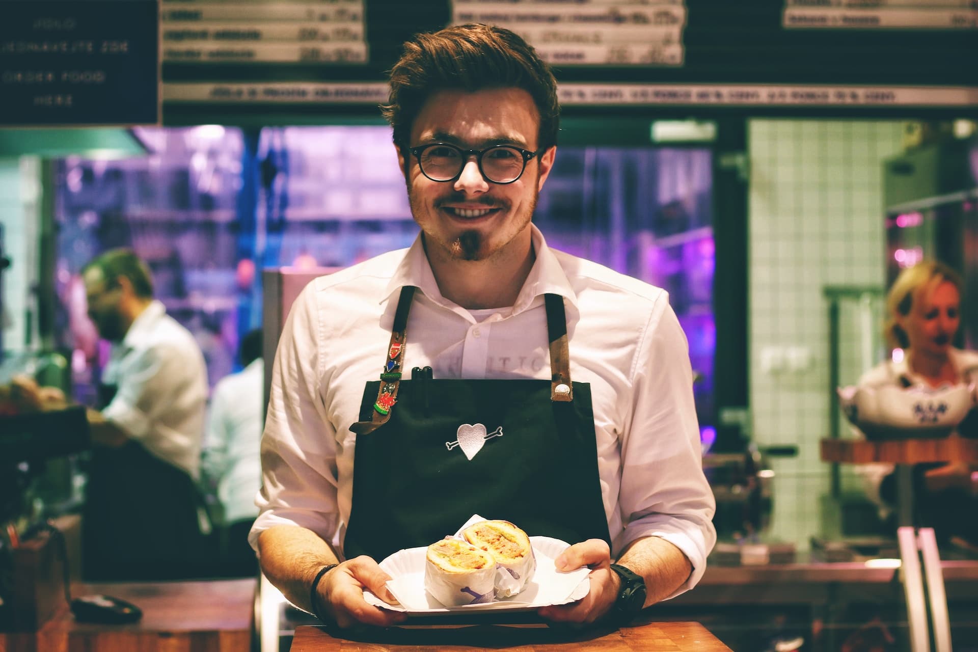 A smiling waiter holding a plate with a sandwich on it