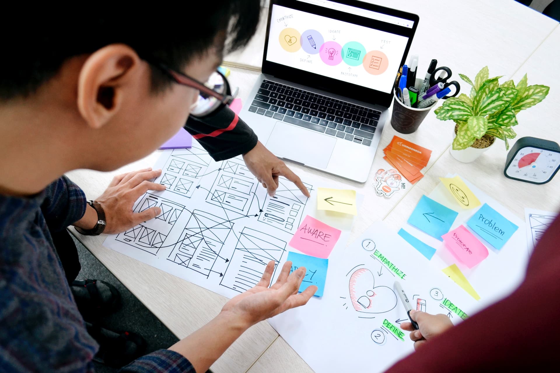 Three team members surrounding a desk filled with project planning papers and a laptop