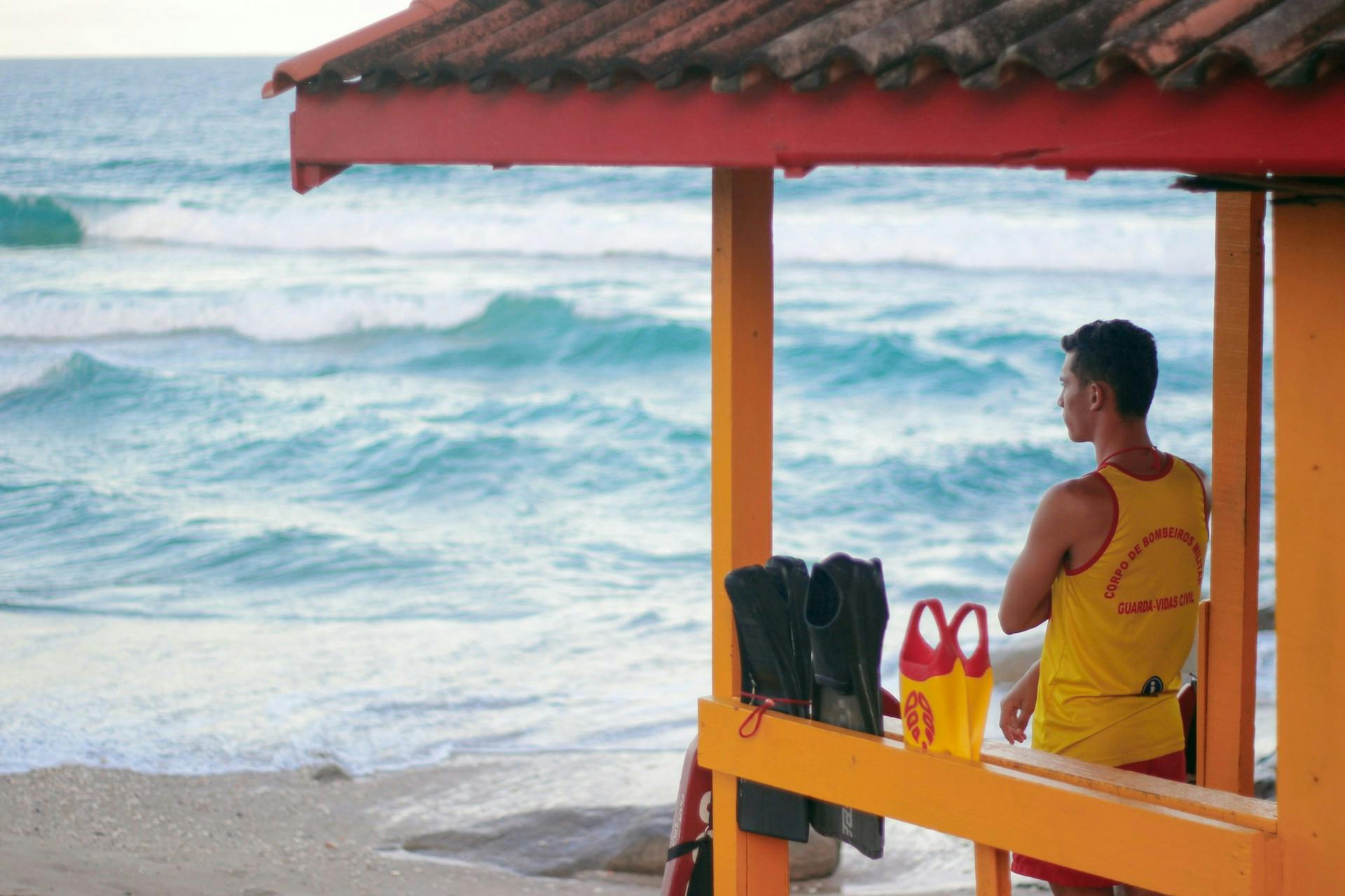 A lifeguard standing at the lifeguard station, looking out at the ocean.