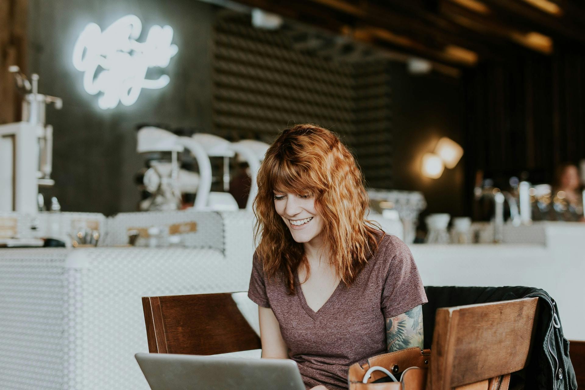 A woman sitting at a coffee shop, smiling at her laptop